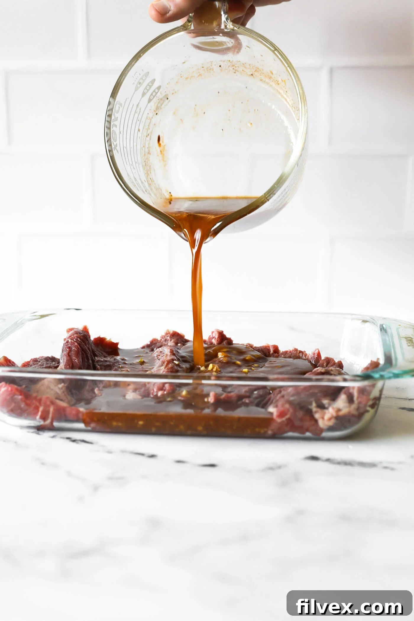 Freshly prepared carne asada marinade being poured over a raw skirt steak laid out in a shallow dish, ensuring complete coverage.