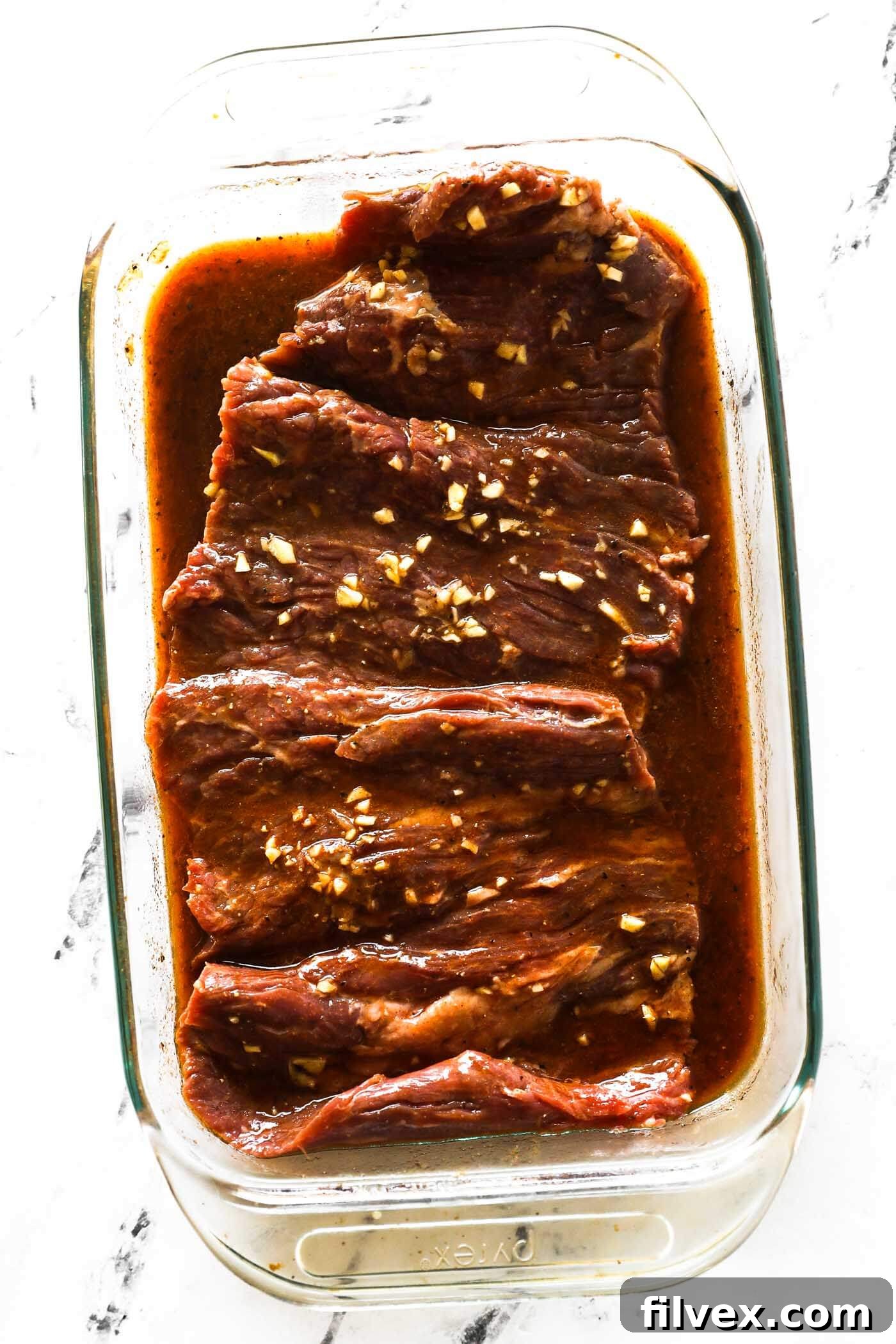 Raw skirt steak submerged in a bright orange citrus marinade, resting in a glass dish, indicating marination time.