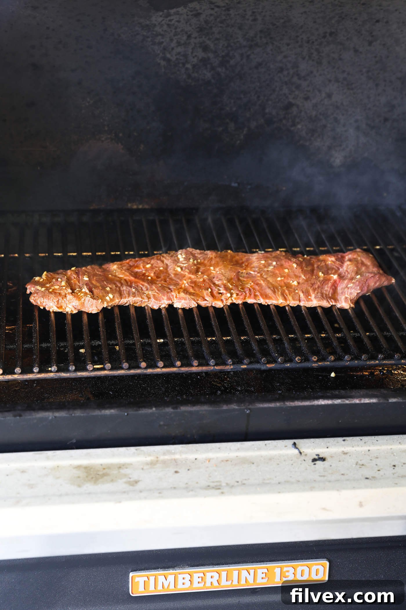 Marinated skirt steak being carefully placed onto a hot grill grate, showing sizzle and grill marks forming.