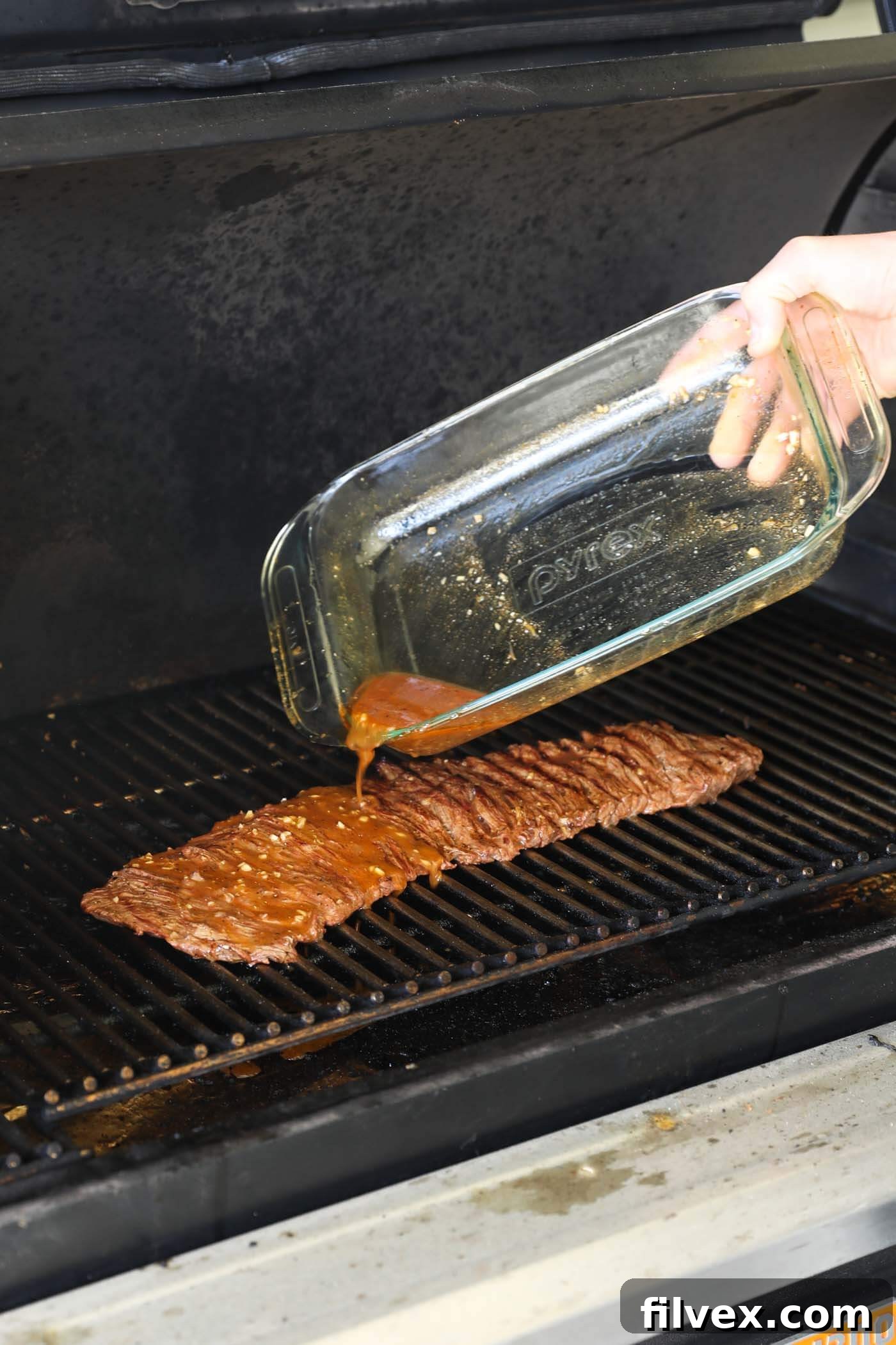 A hand basting grilling carne asada steak with additional marinade using a silicone brush, adding extra flavor during cooking.