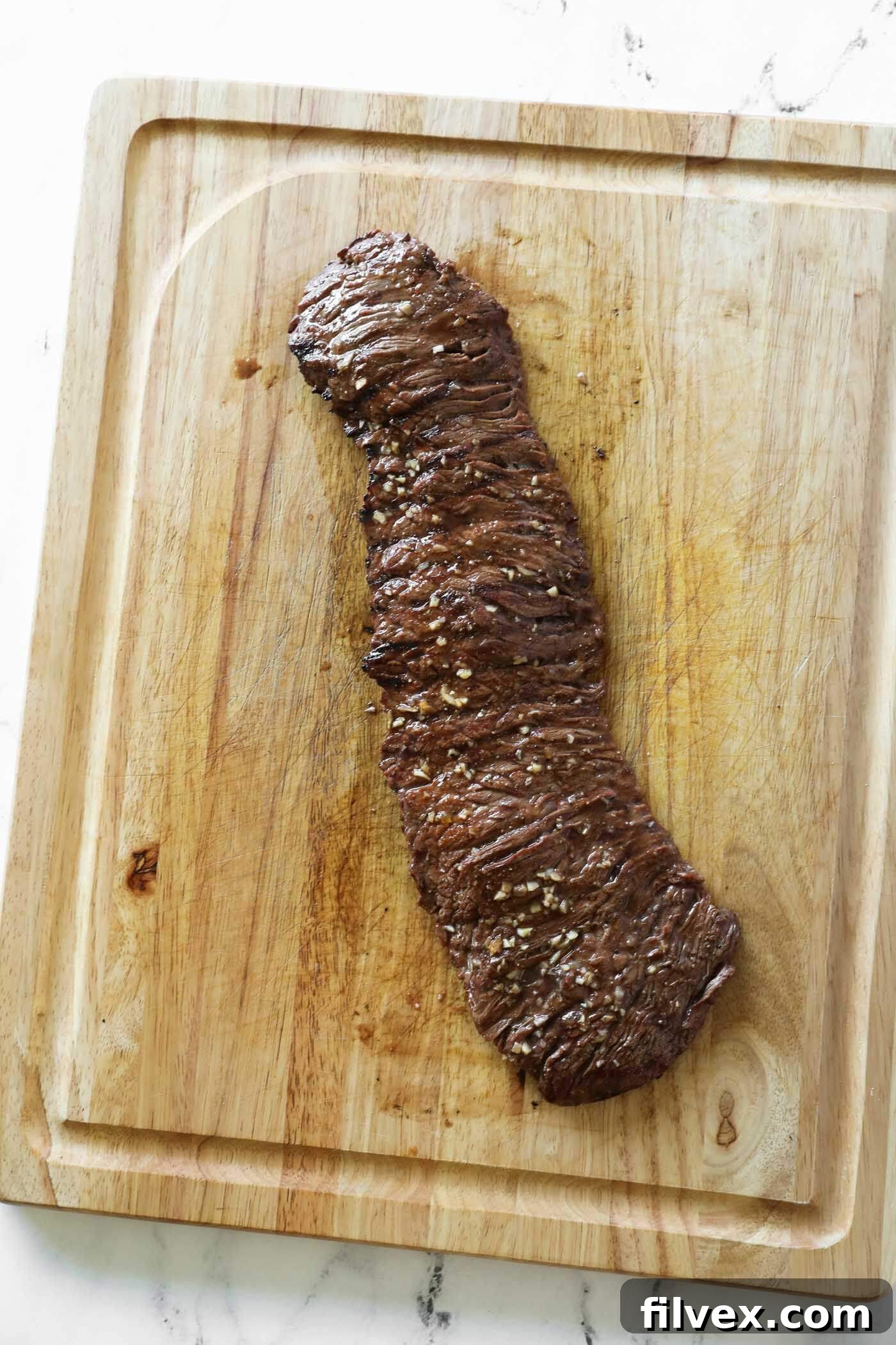 A perfectly cooked carne asada steak resting on a wooden cutting board, having just been removed from the grill.