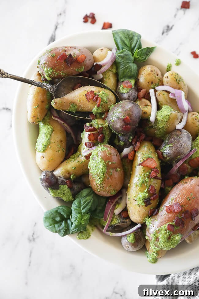 Pesto potato salad in a bowl with a spoon and bacon sprinkled on top, vertical image showcasing freshness.