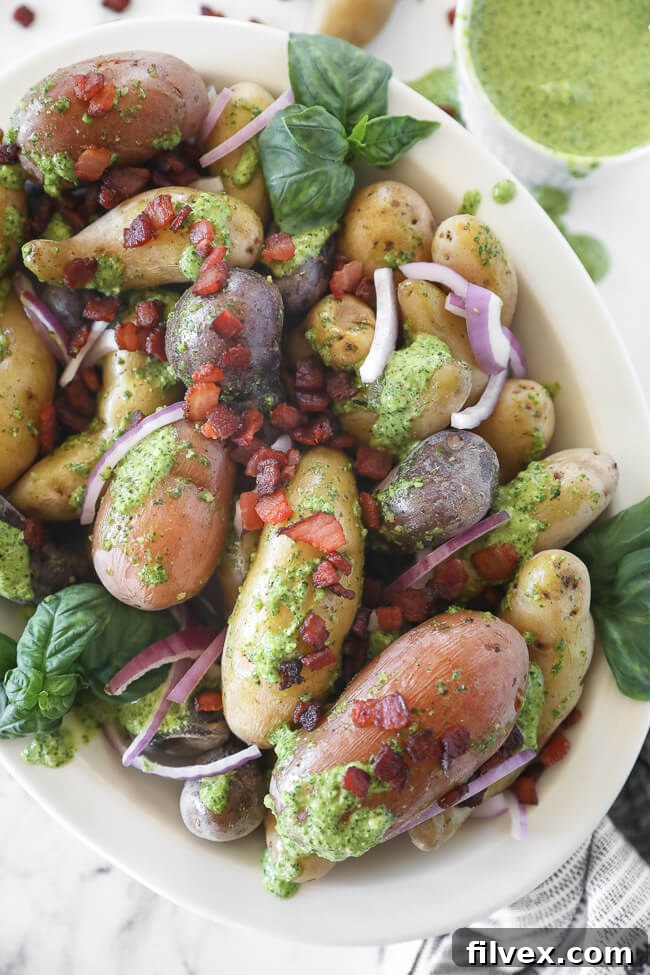Close-up vertical image of pesto potato salad in a bowl with bacon and red onion sprinkled on top, highlighting the textures.