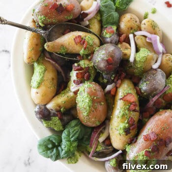 Pesto potato salad in a bowl with a spoon and bacon sprinkled on top, vertical image.