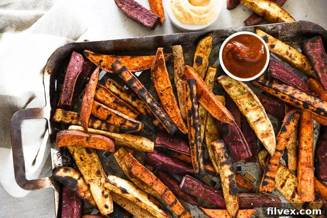 Horizontal overhead image of perfectly grilled sweet potato fries served on a specialized grilling pan, accompanied by small bowls of ketchup and creamy chipotle aioli for dipping. The vibrant colors highlight their fresh appeal.