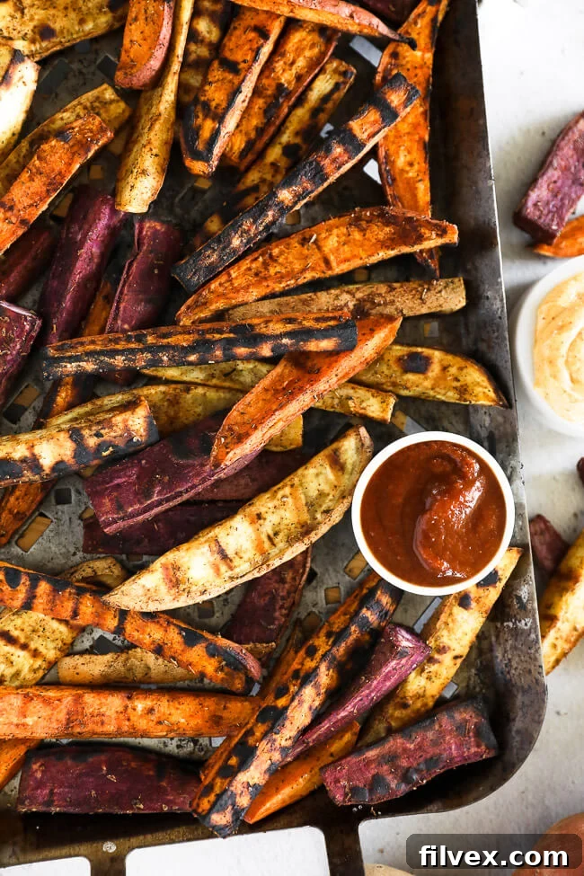 Vertical overhead image of beautifully grilled sweet potato fries arranged on a grilling pan, ready for serving. Ketchup and chipotle aioli are presented in small bowls on the side, inviting a delicious dip.