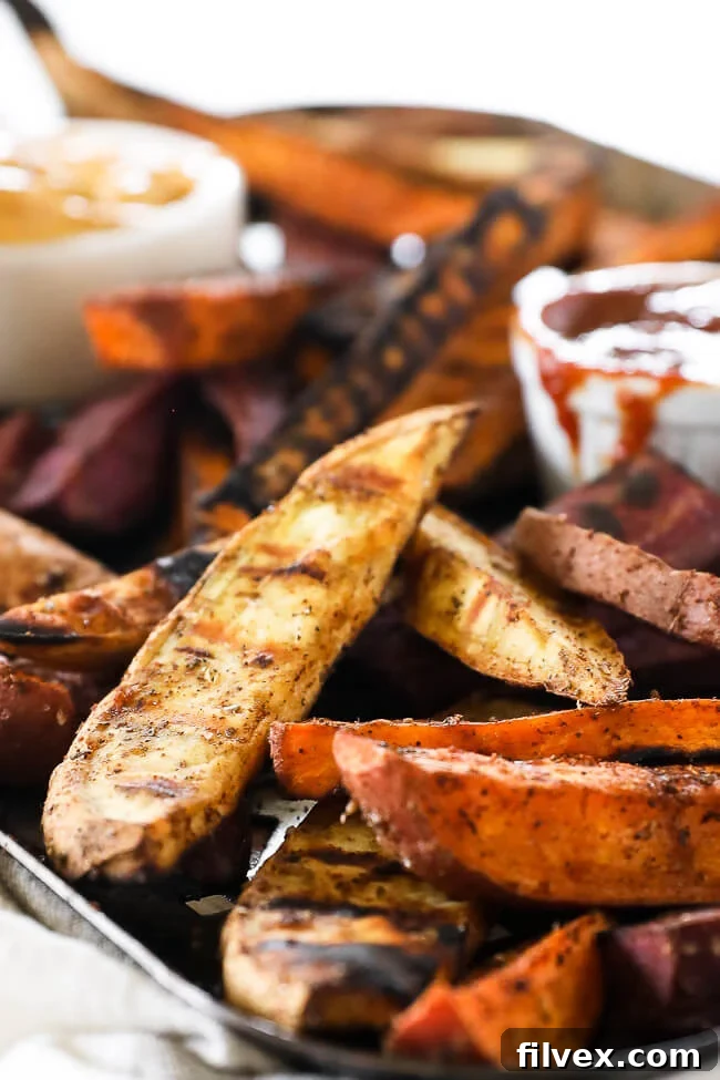 Vertical angled close-up image showcasing a generous serving of grilled sweet potato fries on a dark grilling pan, emphasizing their appealing texture and golden-brown edges.