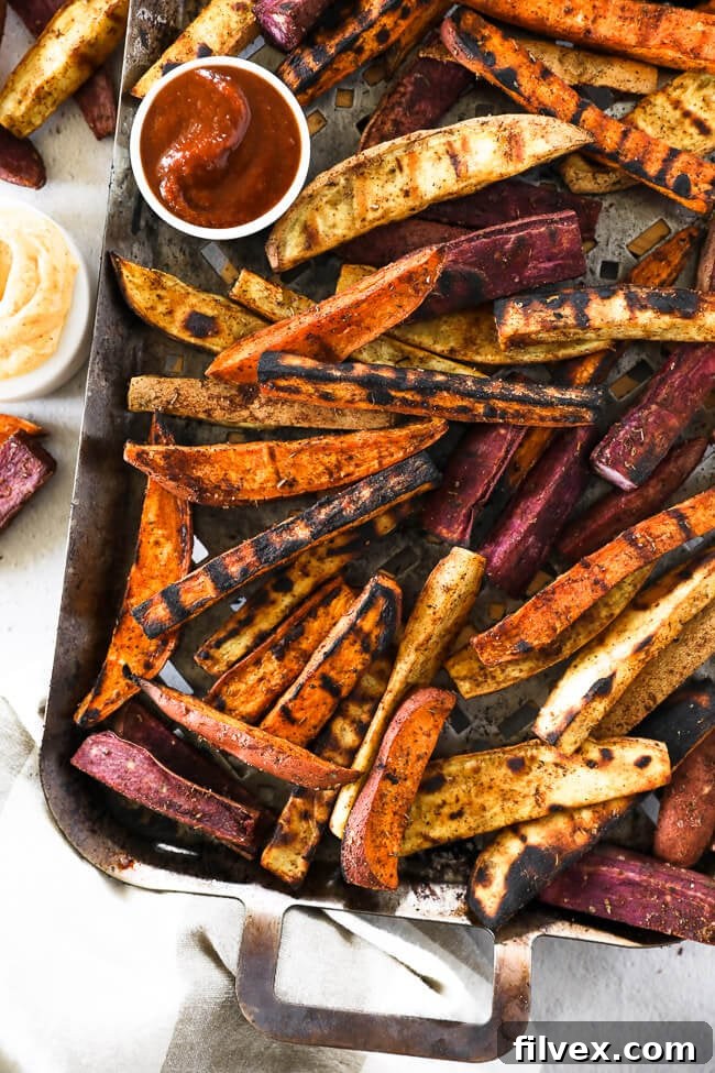 Vertical overhead image of freshly grilled sweet potato fries meticulously arranged on a grilling pan, accompanied by vibrant red ketchup and a creamy chipotle aioli in small dipping bowls.
