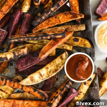 Vertical overhead image of grilled sweet potato fries on a grilling pan with ketchup and chipotle aioli on the side, a perfect summer dish.