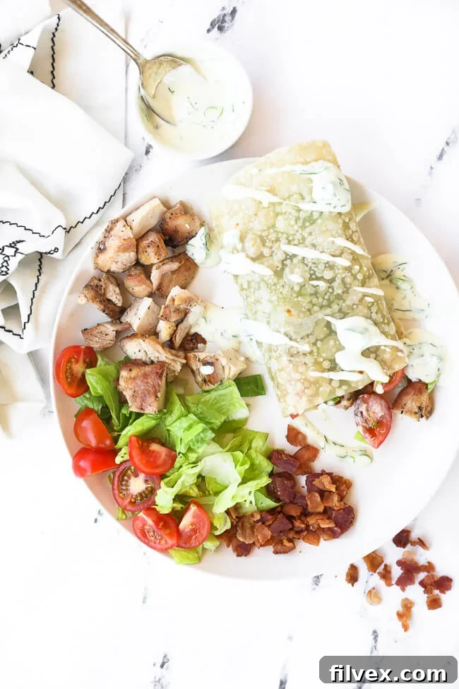Overhead view of a single chicken ranch wrap on a plate with extra ranch drizzle and ingredients like chicken, lettuce, and bacon on the side, highlighting its freshness.
