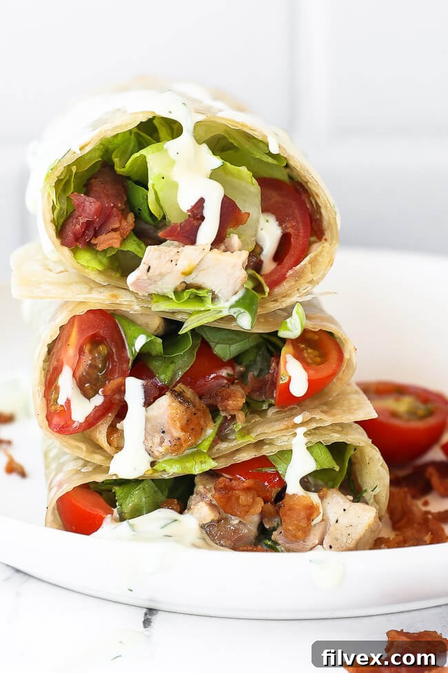 Close-up of stacked grilled chicken bacon ranch wraps, cut in half, with ranch dressing visibly dripping down, emphasizing the creamy texture.