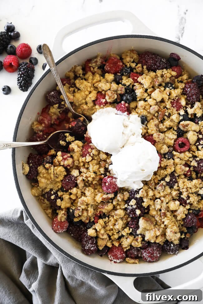 Overhead vertical image of mixed berry crisp in skillet with two spoons dug in and two scoops of ice cream on top. 