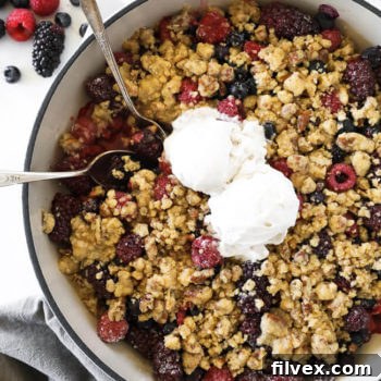 Overhead vertical image of mixed berry crisp in skillet with two spoons dug in and two scoops of ice cream on top.