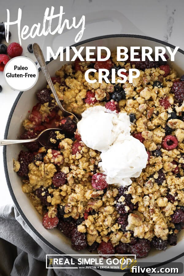 Overhead vertical image of mixed berry crisp in skillet with two spoons dug in and two scoops of ice cream on top. Text overlay at top. 