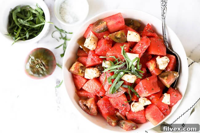 Tomato watermelon salad in a bowl with a serving spoon. Topped with fresh chopped basil. 