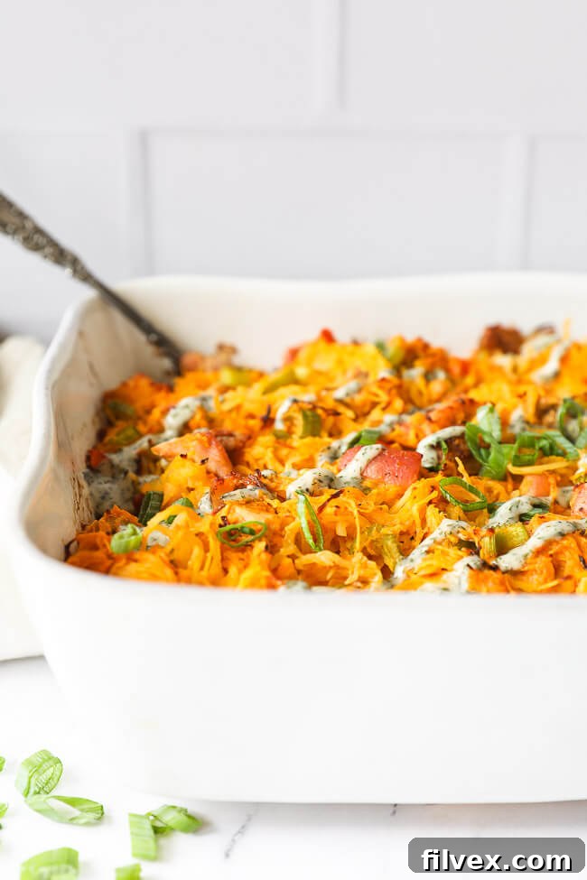 Vertical angled shot of buffalo chicken casserole in casserole dish with chopped green onion and ranch drizzled on top, highlighting the vibrant colors and hearty texture.