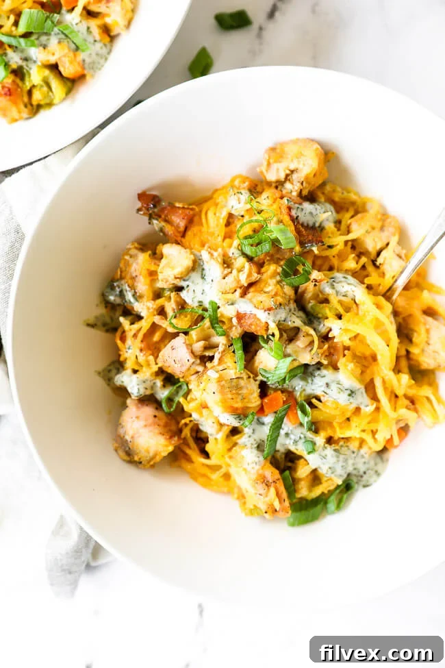 Vertical overhead close up image of buffalo chicken casserole served up in a bowl with a fork dug in, showcasing the strands of spaghetti squash and chicken chunks.