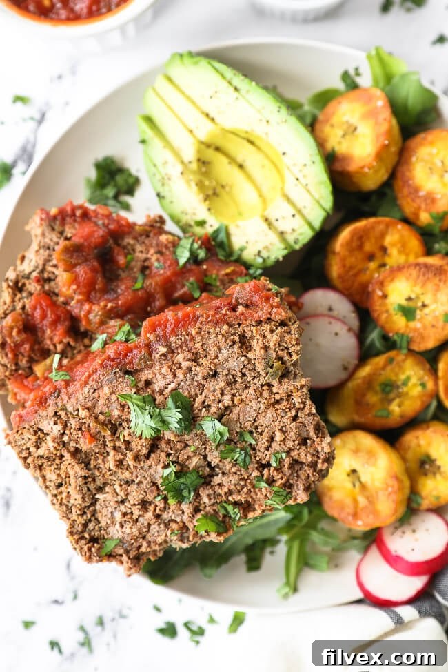Close up vertical image of Mexican meatloaf slices on a plate with avocado, greens, and plantains, showing a complete meal.