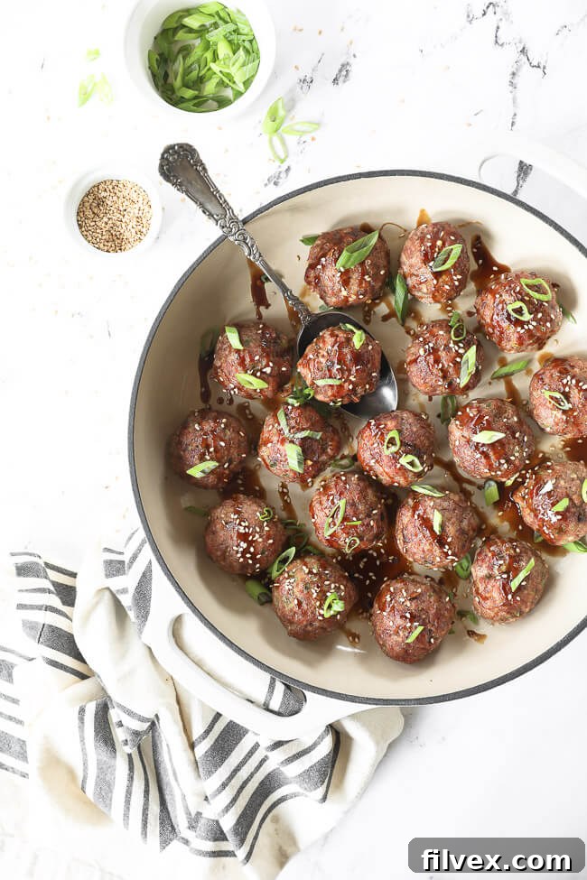Close-up of baked Asian pork meatballs in a skillet, garnished with sauce, green onions, and sesame seeds, ready to be served.