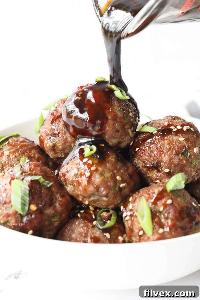 Vertical shot of a rich, glossy sauce being poured over a bowl of Asian pork meatballs, highlighting their delicious coating.