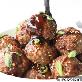 Vertical angled shot of pouring sauce over a bowl of asian meatballs. 