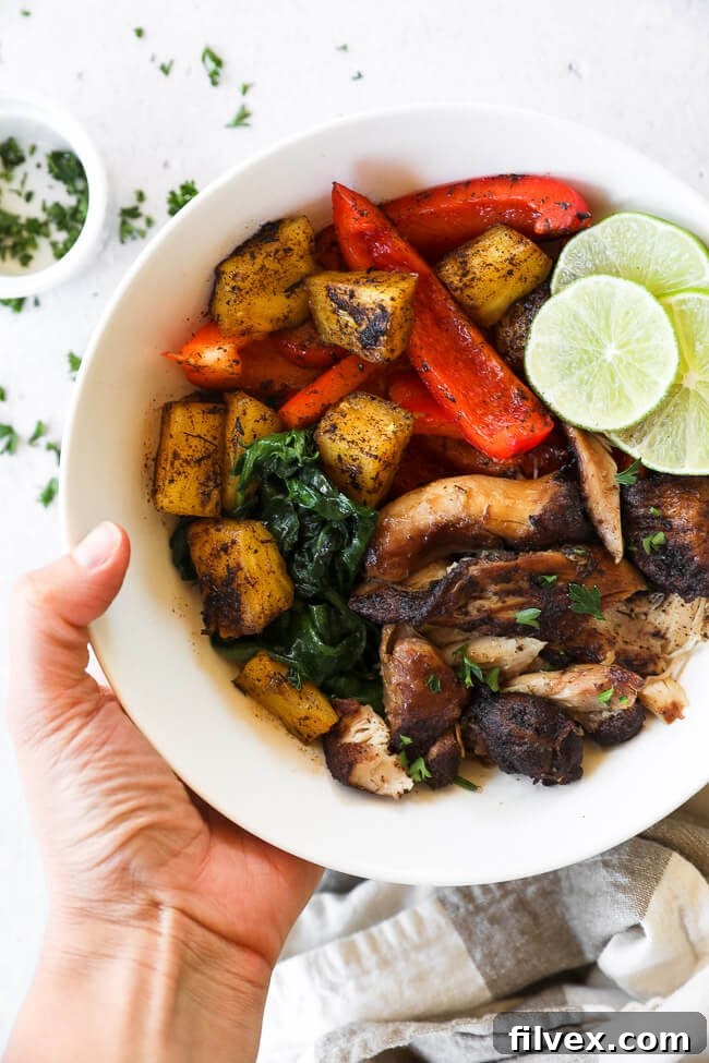 Shredded Jerk chicken in a bowl with vibrant pineapple chunks, fresh greens, bell pepper, and a wedge of lime, held by a hand.