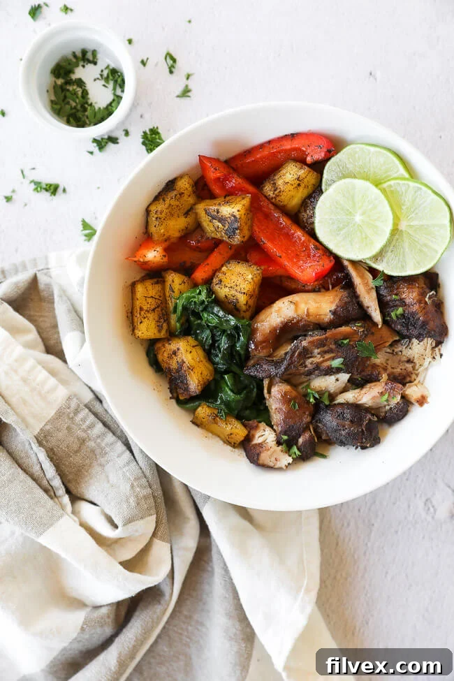 Shredded Jerk chicken in a bowl adorned with fresh pineapple, vibrant greens, bell pepper slices, lime, and a garnish of cilantro.