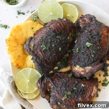 Easy slow cooker jerk chicken on a plate with pineapple and lime, shown in a vertical image.