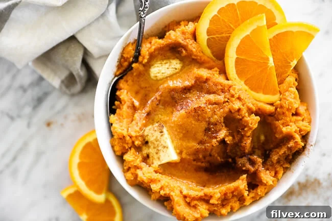 Horizontal overhead image of Thanksgiving yams in a bowl with a serving spoon. Melted butter and cinnamon on top with orange slices as a garnish. 