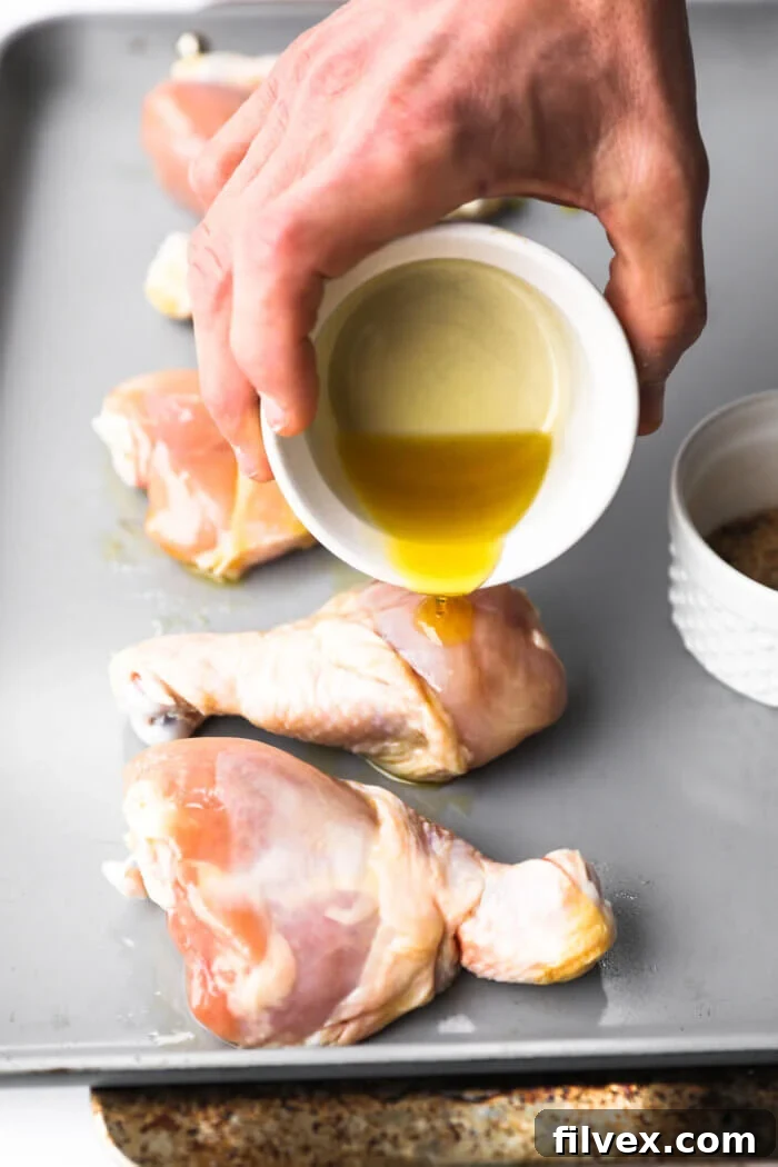 Chicken drumsticks being drizzled with oil on a cutting board.