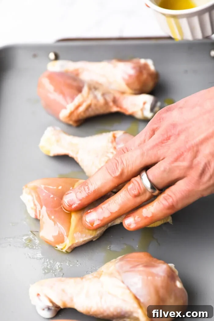 Hands rubbing oil over chicken drumsticks to coat them evenly.