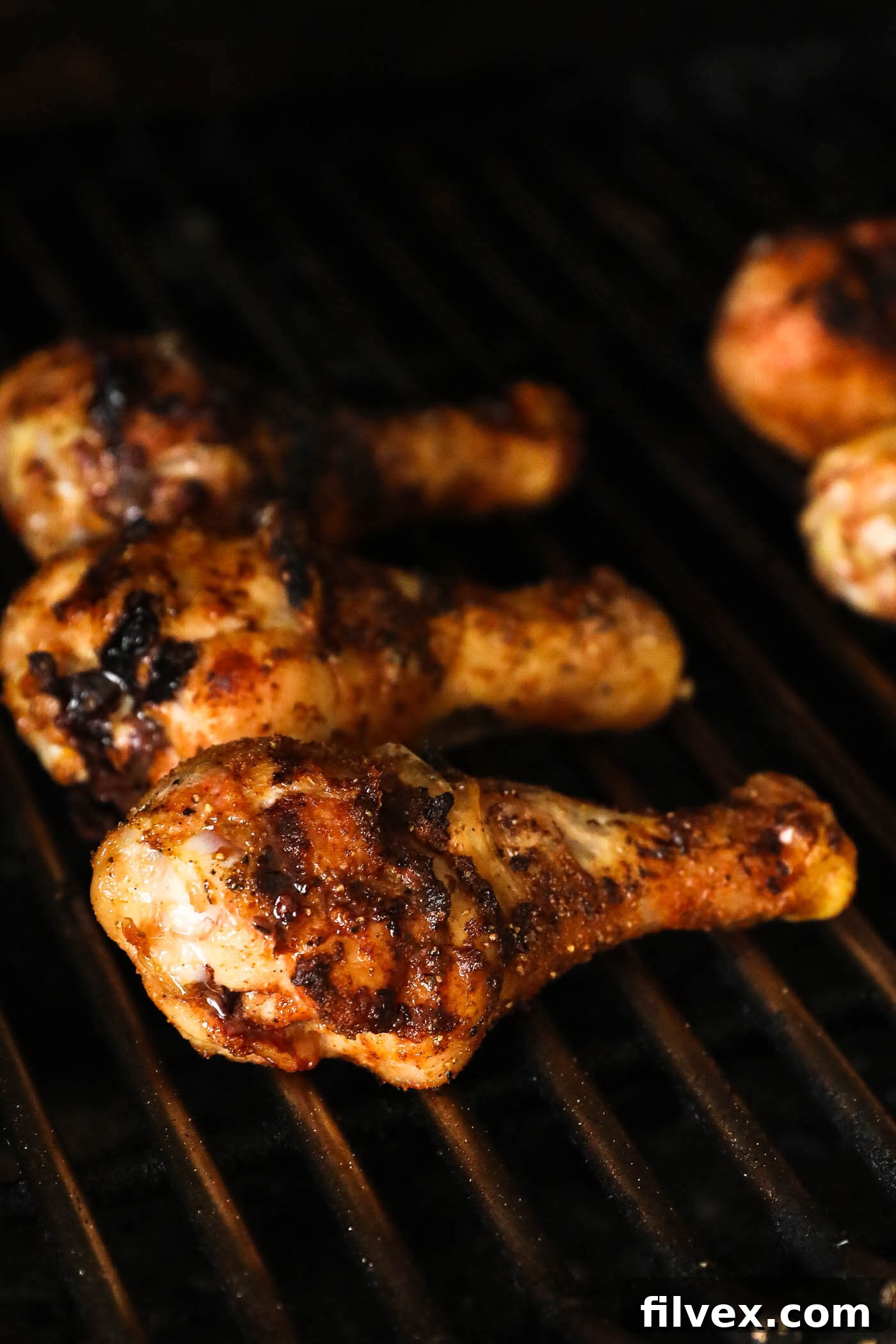 Grilled chicken drumsticks cooking on a barbecue, showing smoke and grill marks.