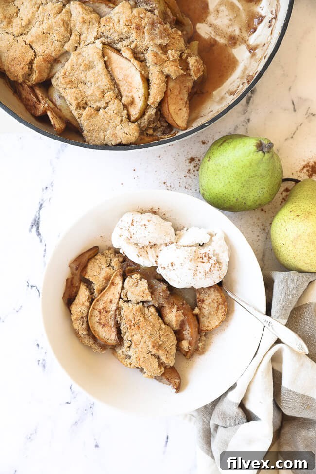Vertical overhead image of pear cobbler served in a bowl with two scoops of ice cream and a spoon. 