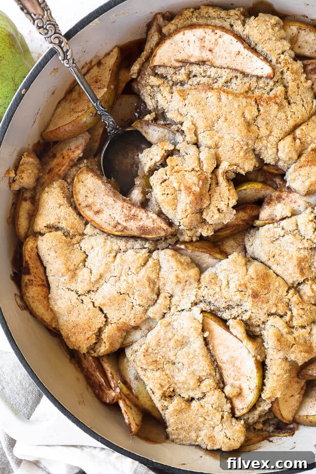 Vertical overhead close up image of pear cobbler in a skillet with a serving spoon dug in. 