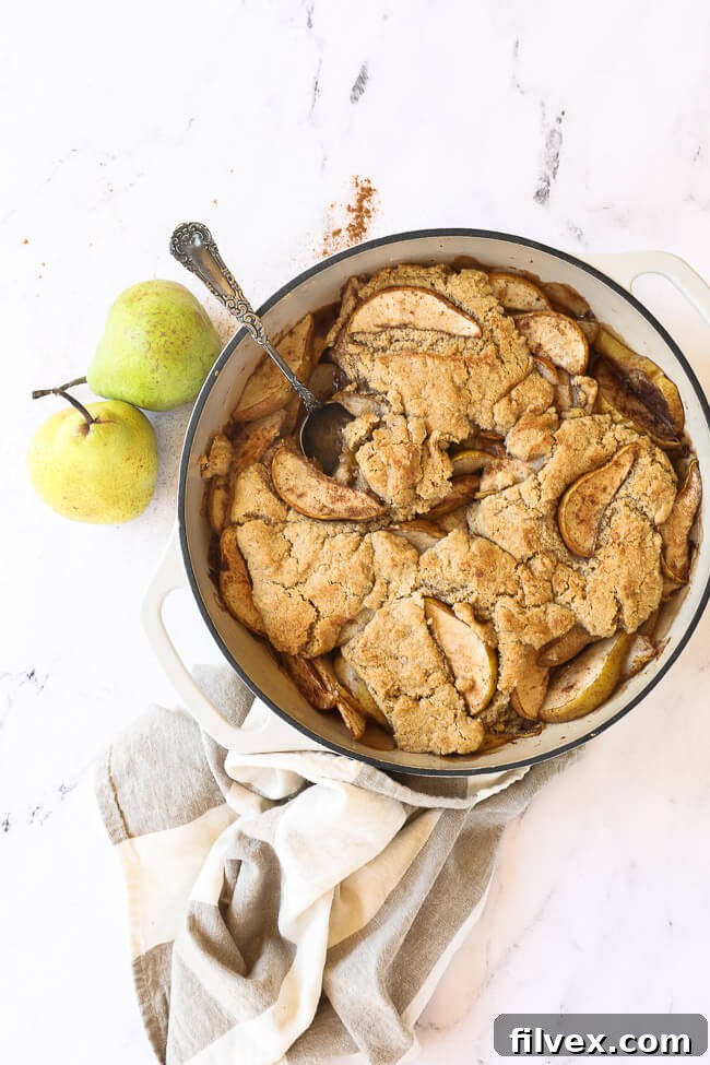 Pulled out vertical image of pear cobbler in skillet with serving spoon. 