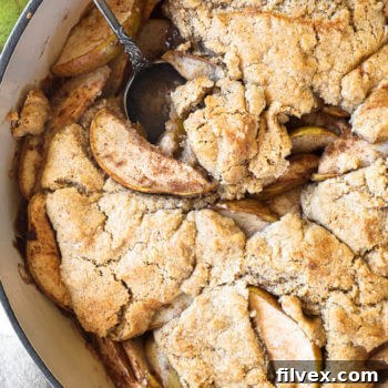 Vertical overhead close up image of pear cobbler in a skillet with a serving spoon dug in.