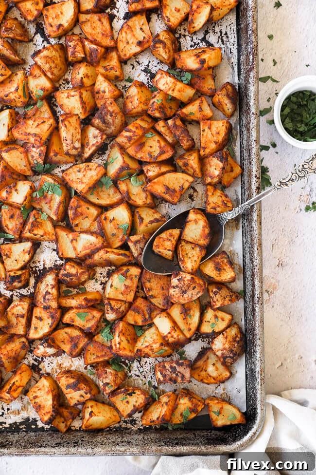 Sheet pan filled with golden-brown, crispy oven roasted Spanish potatoes, with a serving spoon resting among them, ready to be enjoyed.
