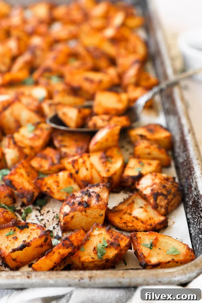 Close-up view of golden-brown crispy oven roasted Spanish potatoes on a sheet pan, showing the delightful texture and seasoning, with a spoon digging in.