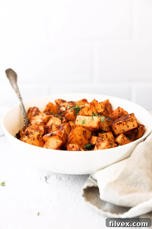 A bowl of crispy oven roasted Spanish potatoes with a serving spoon, presented straight on, showcasing their appeal as a delicious side dish.