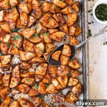 Crispy oven roasted Spanish potatoes on a sheet pan with a spoon in potatoes