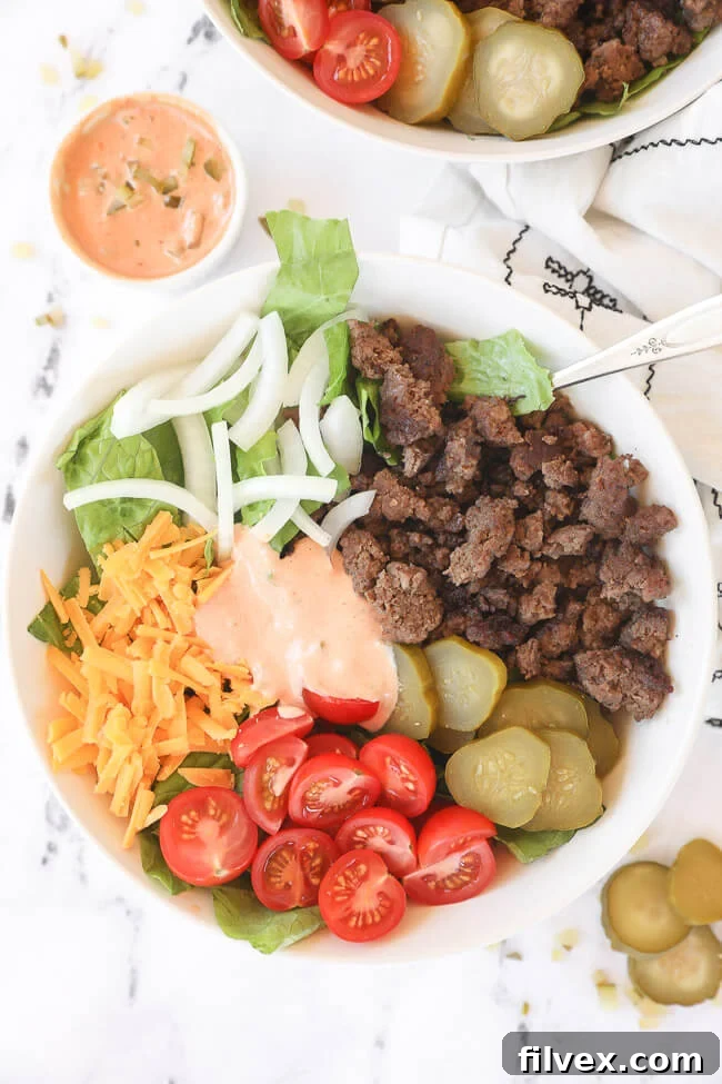 Big mac salad in a bowl with ground beef, cheese, tomato, pickle, onion and sauce in middle.