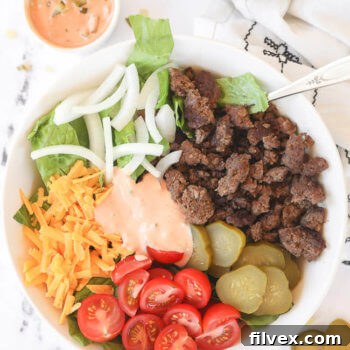 Big mac salad in a bowl with ground beef, cheese, tomato, pickle, onion and sauce in middle.