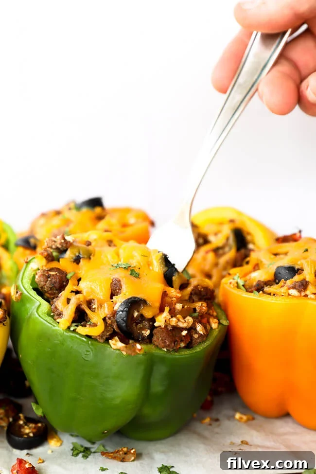 Close up straight on shot of stuffed bell peppers topped with melted cheddar cheese and a fork going into one pepper