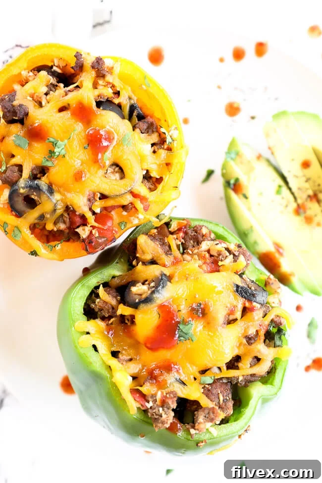 2 stuffed bell peppers topped with melted cheddar cheese and hot sauce on a plate with avocado
