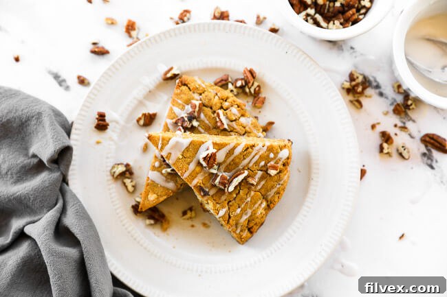 Two gluten-free vegan pumpkin scones on a plate with chopped pecans and icing on top.
