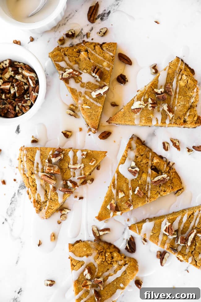 Vertical image of gluten-free and vegan pumpkin scones spread out on marble with icing drizzled on top and sprinkled with chopped pecans.