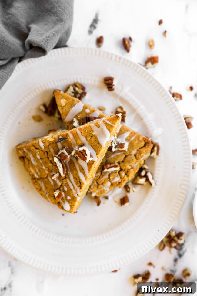 Vertical image of two gluten-free and vegan pumpkin scones stacked on a plate with icing and chopped pecans on top.