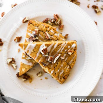 Vertical image of two gluten-free and vegan pumpkin scones stacked on a plate with icing and chopped pecans on top.