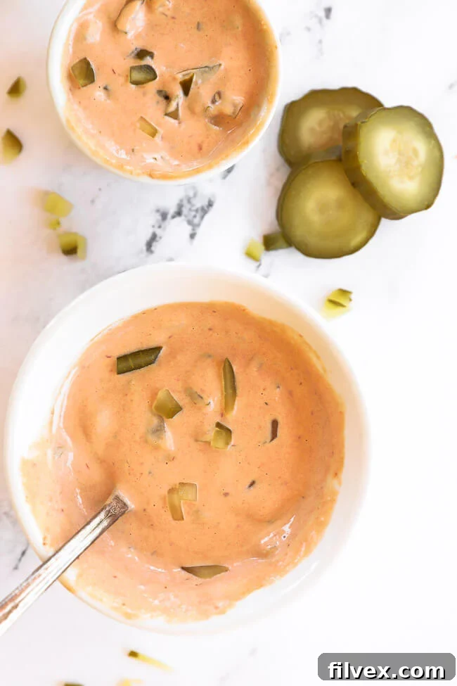 Two small ramekins filled with creamy Big Mac sauce, garnished with fresh dill sprigs, surrounded by neatly sliced dill pickles on a rustic wooden board. The scene emphasizes the sauce's fresh ingredients and appealing texture.