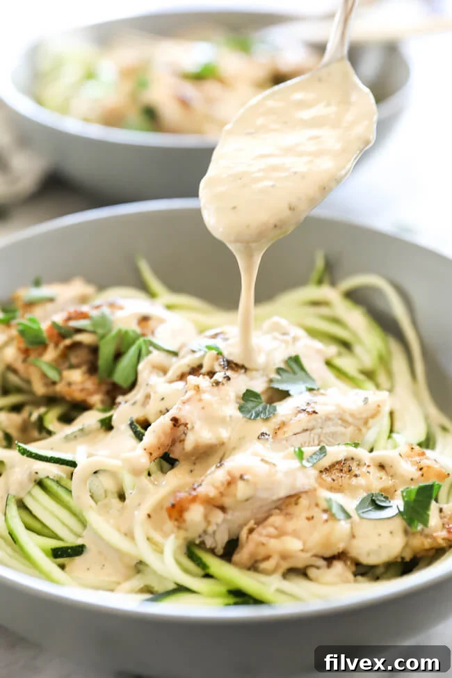 Close up shot of creamy vegan alfredo sauce in a small bowl, garnished with fresh herbs and cracked black pepper.